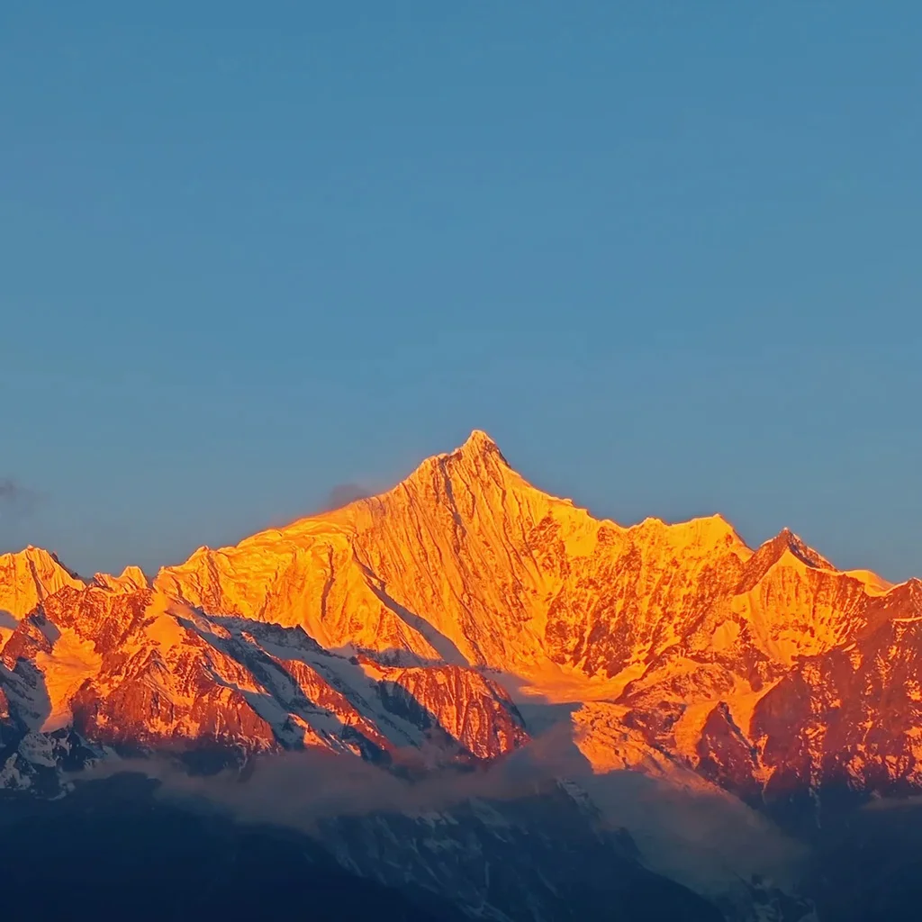 Meili Snow Mountain 清晨陽光照耀 梅里雪山,雪峰被金色光芒染亮,山體輪廓清晰壯麗,天空湛藍,呈現震撼的「日照金山」自然奇觀。