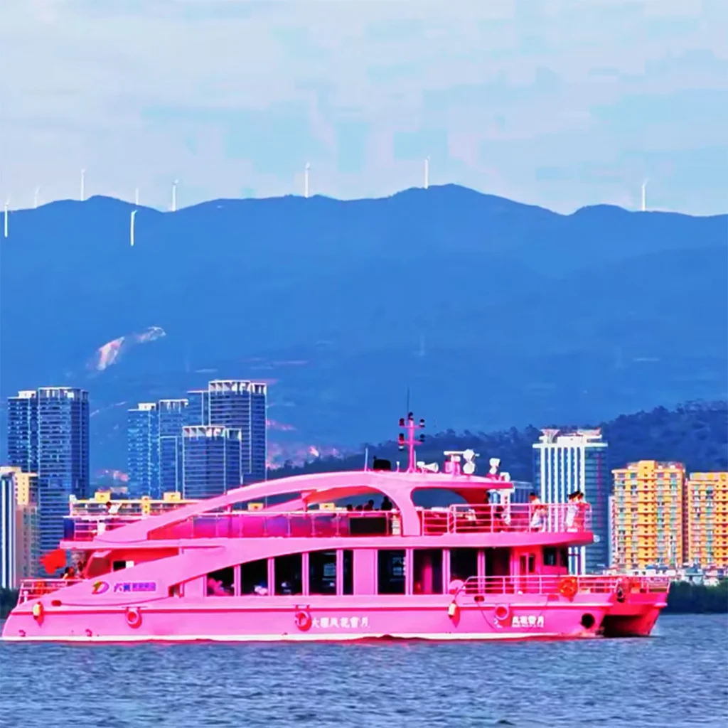 在 洱海 湖面上，一艘粉色遊艇緩緩航行，背景為大理城市建築與遠山景觀。
