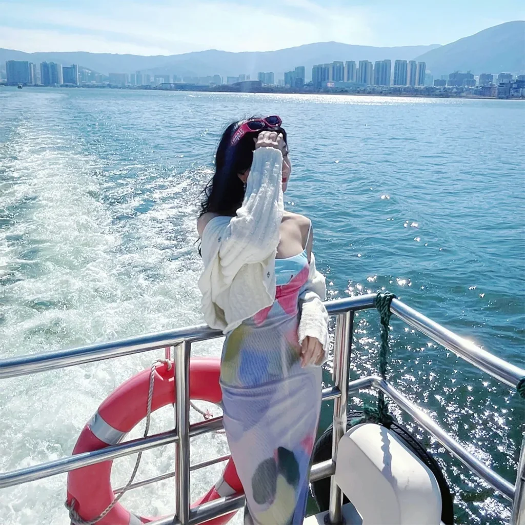 在 洱海 遊艇甲板上，一名女子迎著湖風站立，身後水花翻湧，遠方城市與群山相映。
