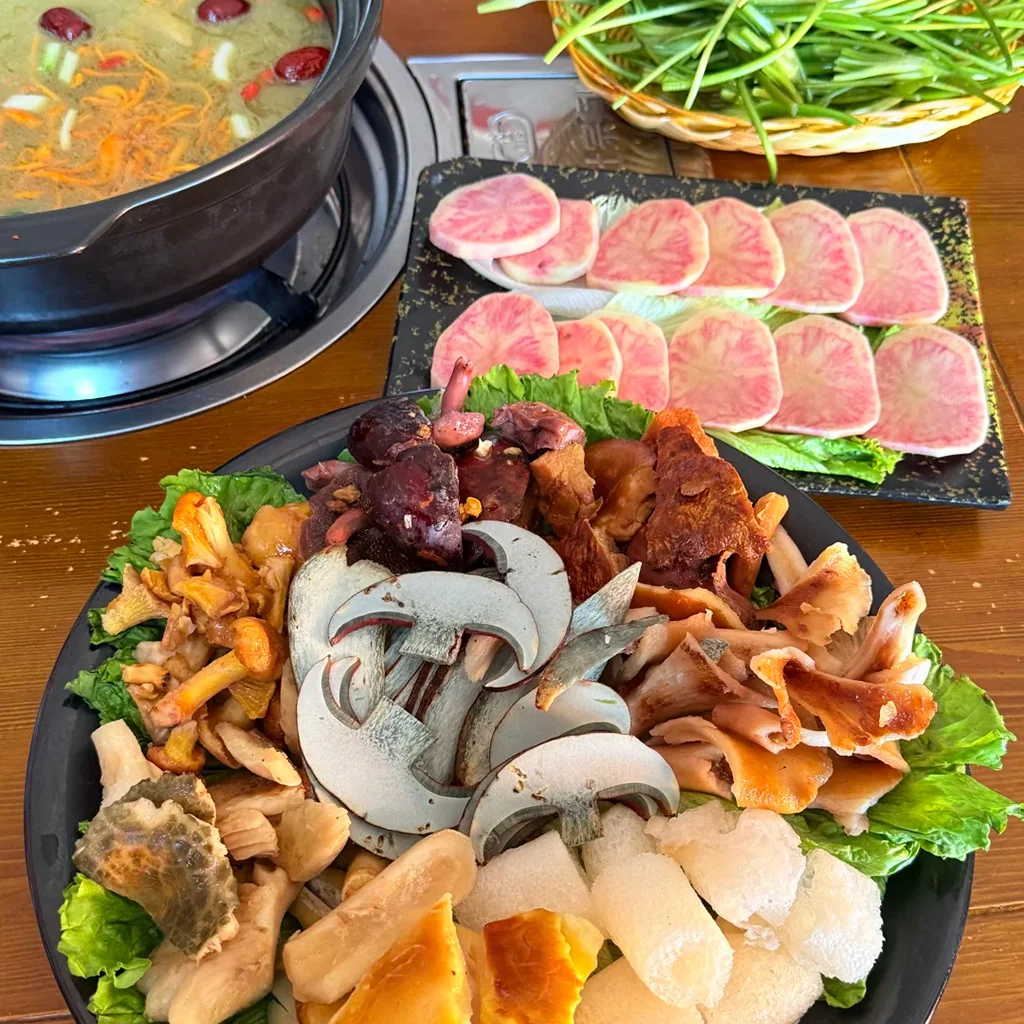 Wild mushroom hot pot 黑色大盤中擺放著多種新鮮野生菌切片,配上一鍋沸騰的高湯與粉紅色蘿蔔片,展現道地雲南風味。