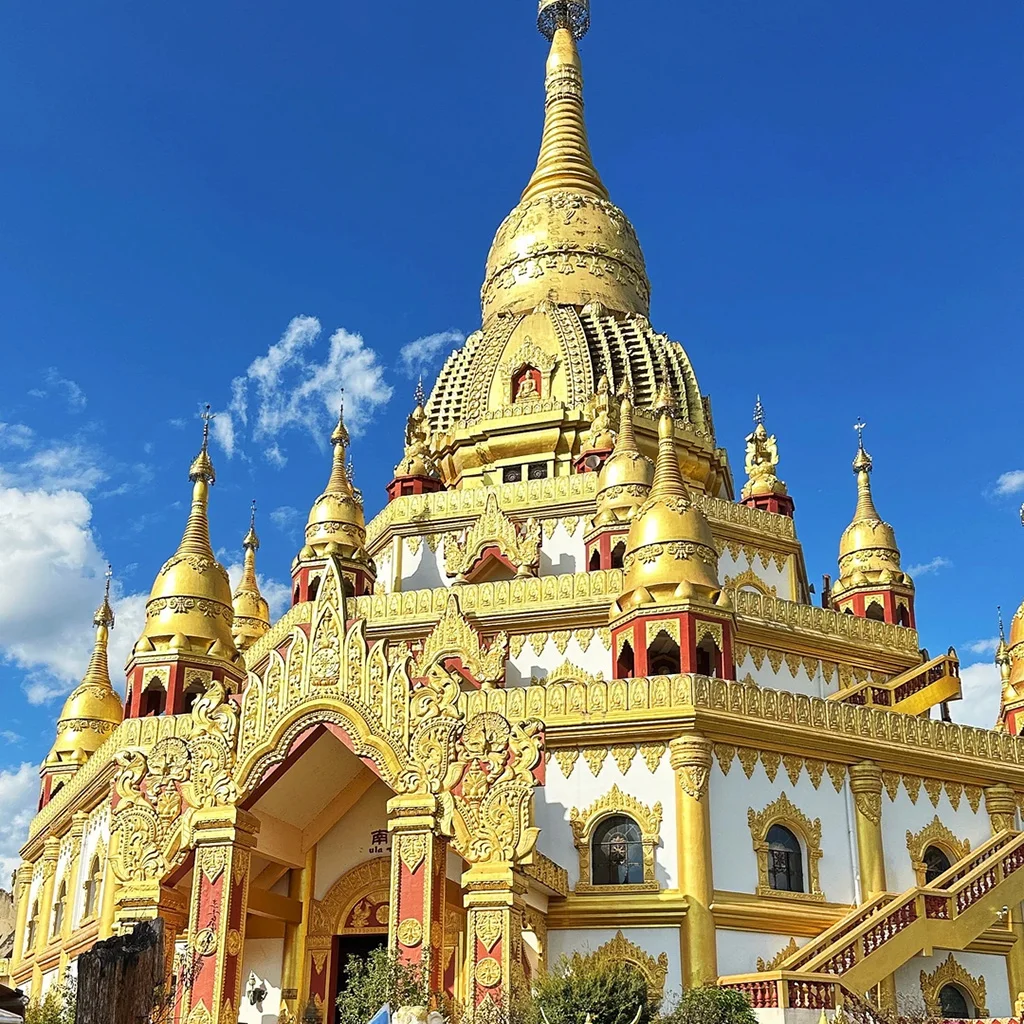 Meng Huan Grand Golden Pagoda 中國雲南芒市勐煥大金塔,宏偉鍍金佛塔,精緻雕刻與聳立尖塔,背景是澄澈藍天。