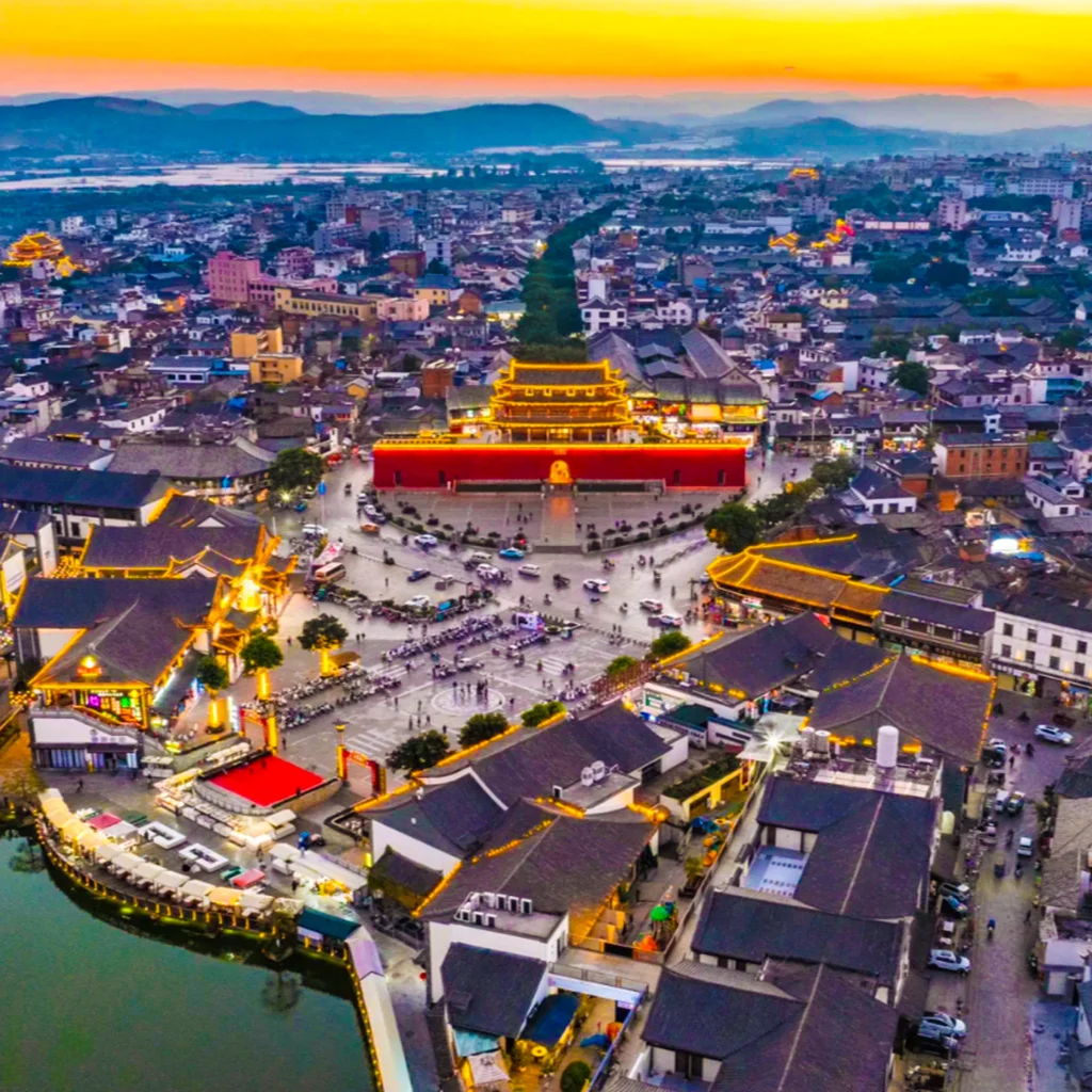 Jianshui Ancient City 雲南建水古城黃昏城市景觀,空拍視角可見城門與古建築在燈光點綴下格外醒目,街道向四方延伸,周圍傳統屋頂與現代城市交織,展現建水古城歷史文化與熱鬧生活交融的景象。