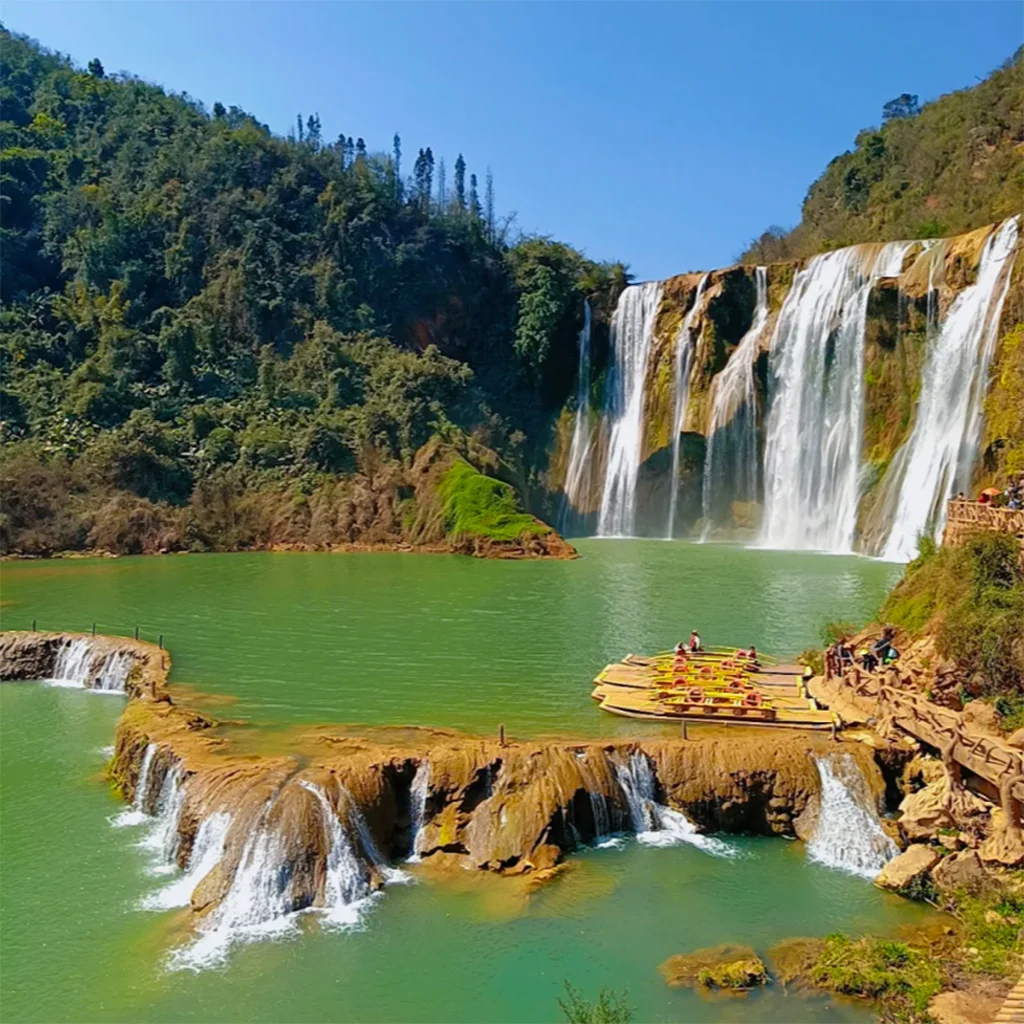 Jiulong Waterfall 壯觀的瀑布景觀位於 九龙瀑布群。多條瀑布從高崖傾瀉而下,落入綠色湖水中,前景可見層疊小瀑布與木筏遊船,四周山林環繞。