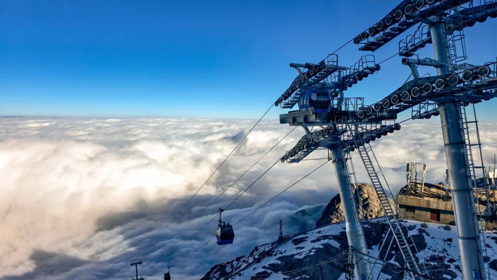 Jade Dragon Snow Mountain Glacier Cableway 1 雲南麗江玉龍雪山冰川大索道,纜車飛馳於雲海之上,巨型鋼塔聳立,背景是積雪覆蓋的山巔。
