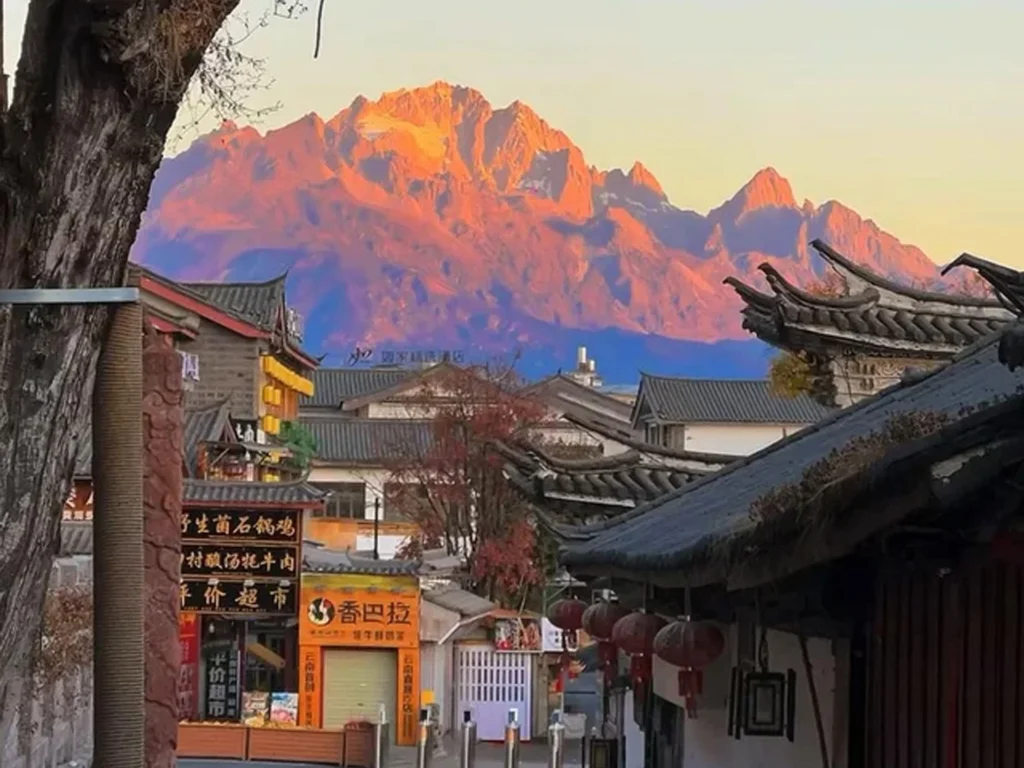 麗江古城眺望玉龍雪山的絕美「機位」，清晨日出時刻，雪山被金紅霞光染成「日照金山」奇景，前景是古色古香的納西建築。